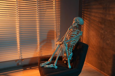 Photo of Waiting concept. Human skeleton sitting in armchair indoors, space for text