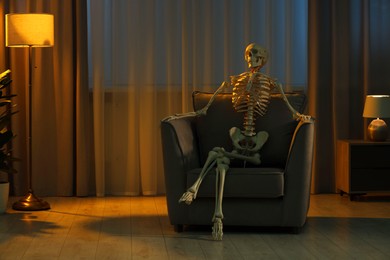 Waiting concept. Human skeleton sitting in armchair at home, space for text