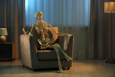 Photo of Waiting concept. Human skeleton sitting in armchair at home, space for text