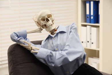 Waiting concept. Human skeleton sitting in armchair at office