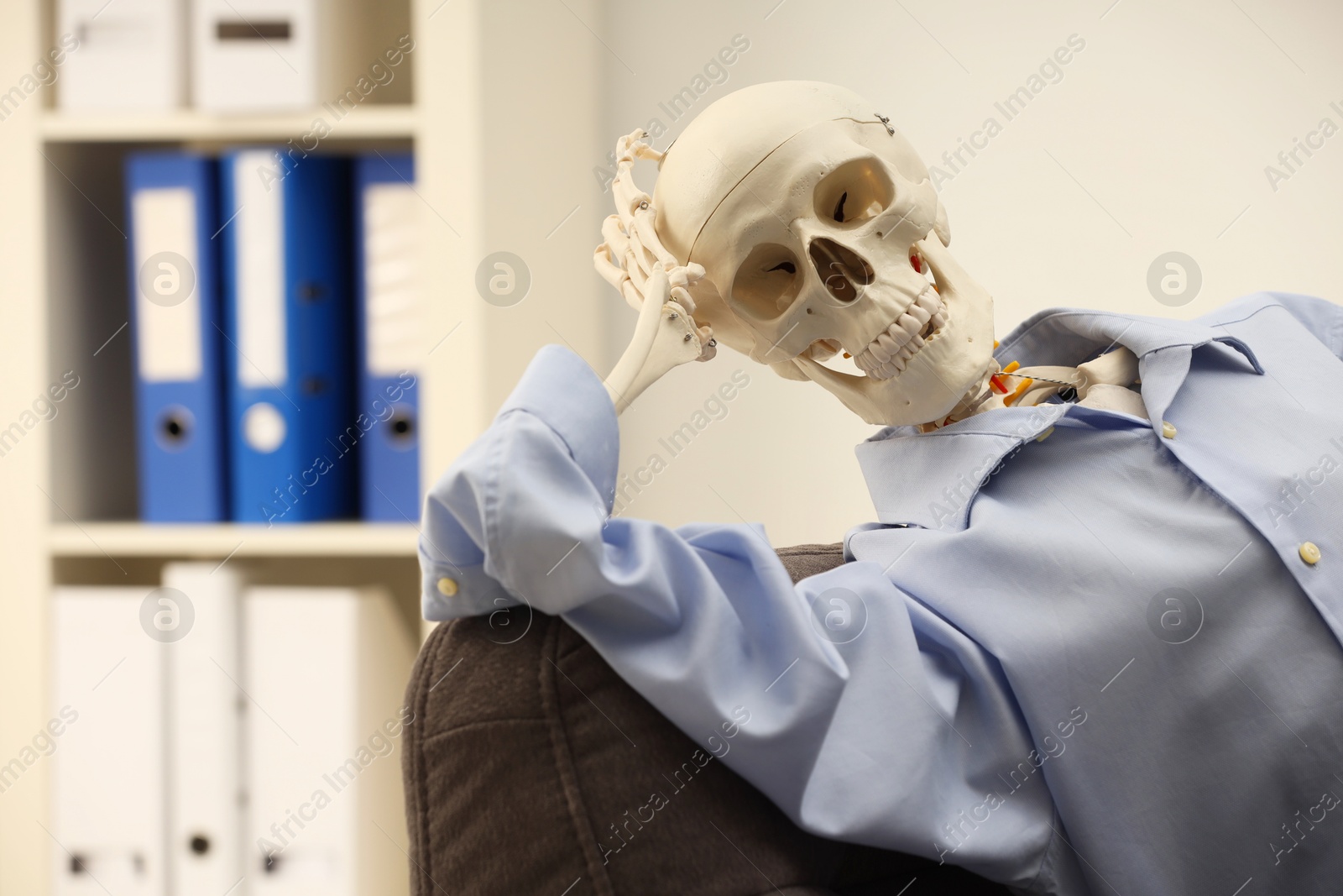 Photo of Waiting concept. Human skeleton sitting in armchair at office