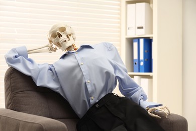 Waiting concept. Human skeleton sitting in armchair at office