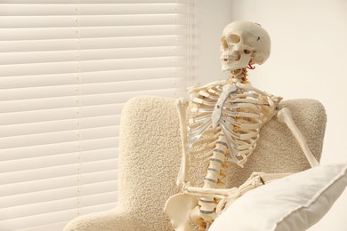 Photo of Waiting concept. Human skeleton sitting in armchair indoors, space for text