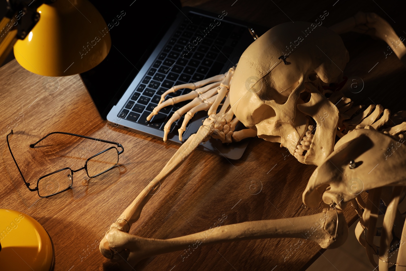 Photo of Waiting concept. Human skeleton sleeping at wooden table with laptop