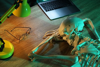 Photo of Waiting concept. Human skeleton sleeping at wooden table with laptop