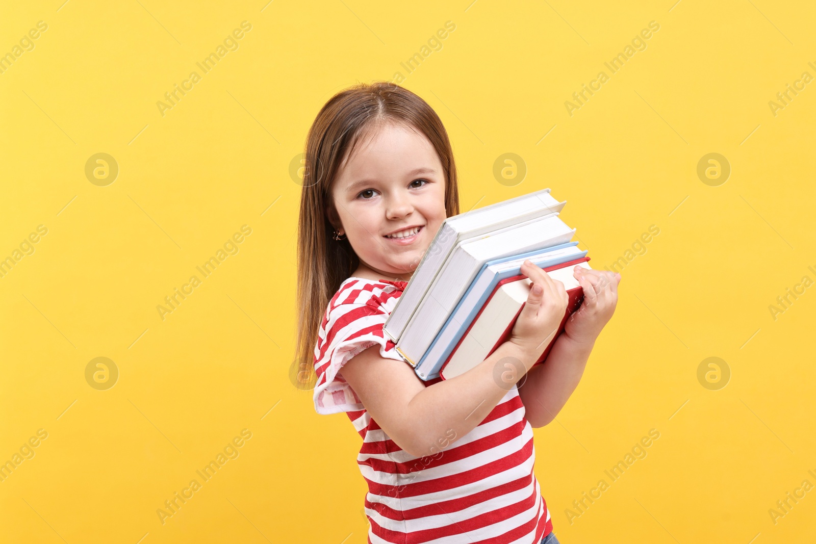 Photo of Cute little girl with books against orange background