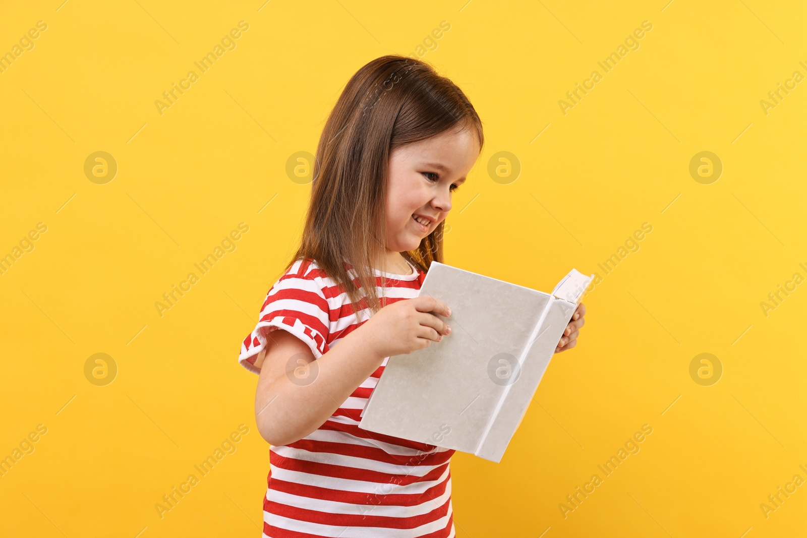 Photo of Cute little girl reading book on orange background