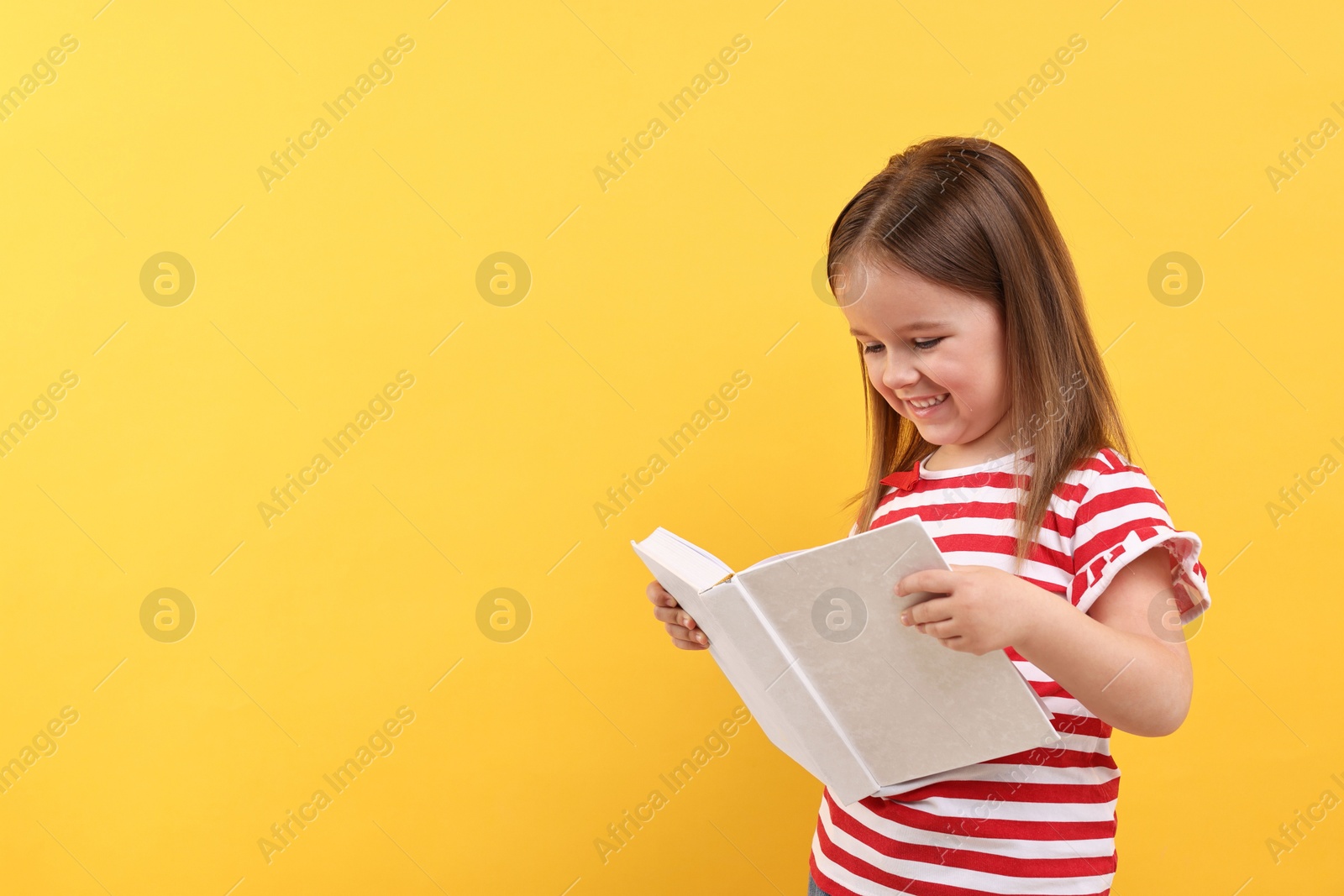 Photo of Cute little girl reading book on orange background. Space for text