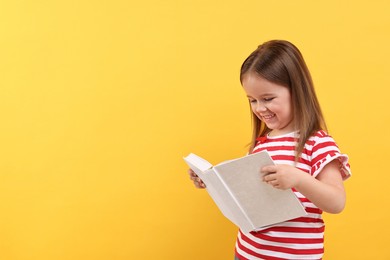 Photo of Cute little girl reading book on orange background. Space for text