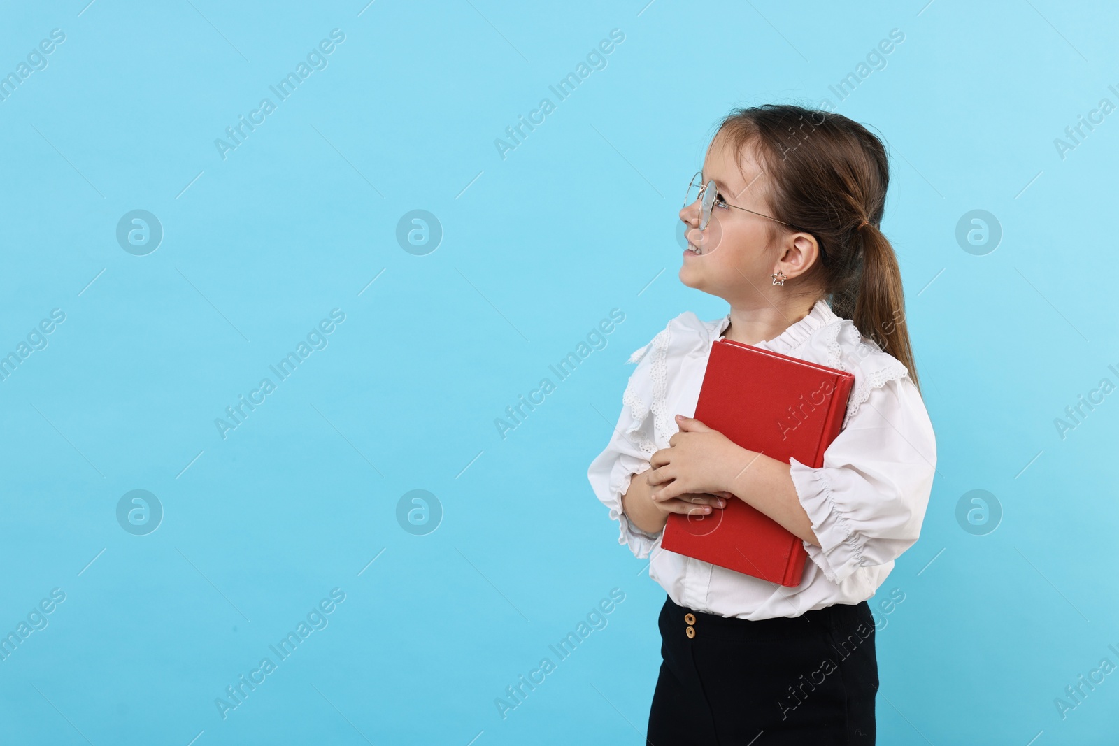 Photo of Cute little girl in glasses with book on light blue background. Space for text