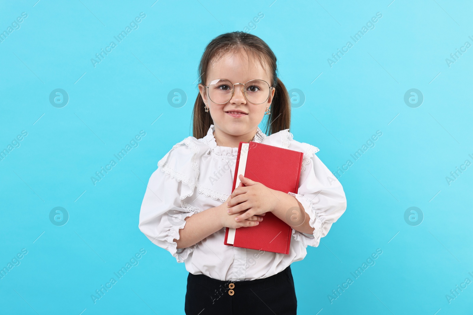 Photo of Cute little girl in glasses with book on light blue background