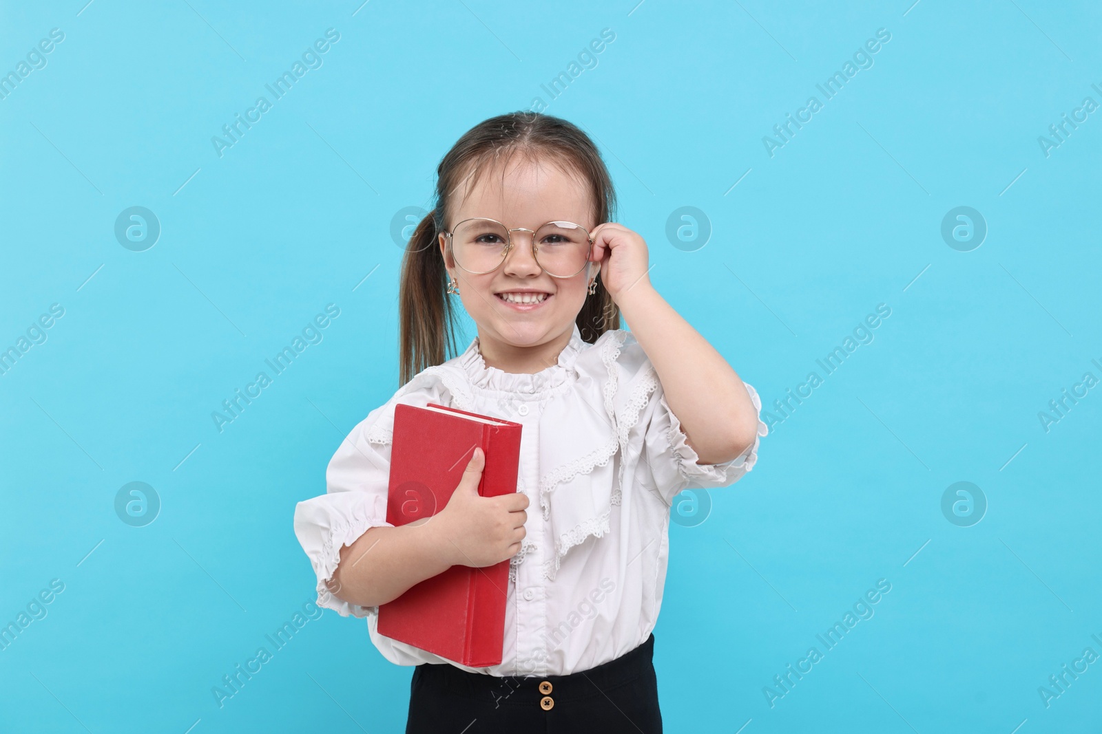 Photo of Cute little girl in glasses with book on light blue background