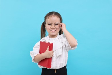 Cute little girl in glasses with book on light blue background