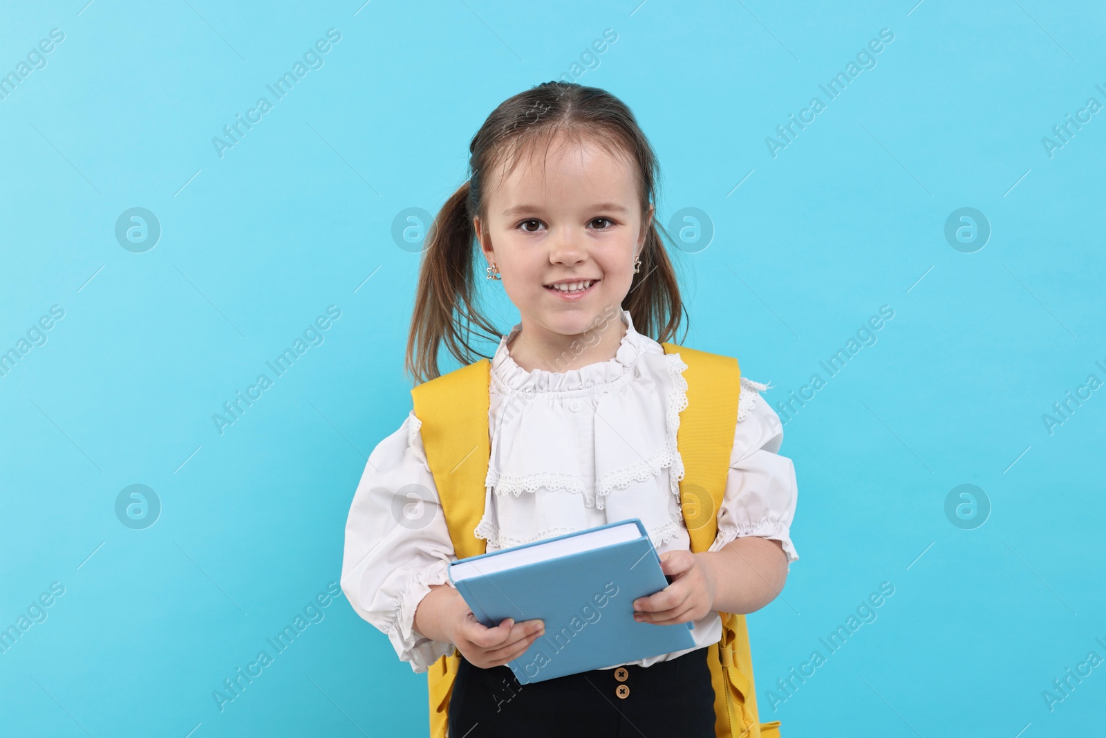 Photo of Cute little girl with book and backpack on light blue background