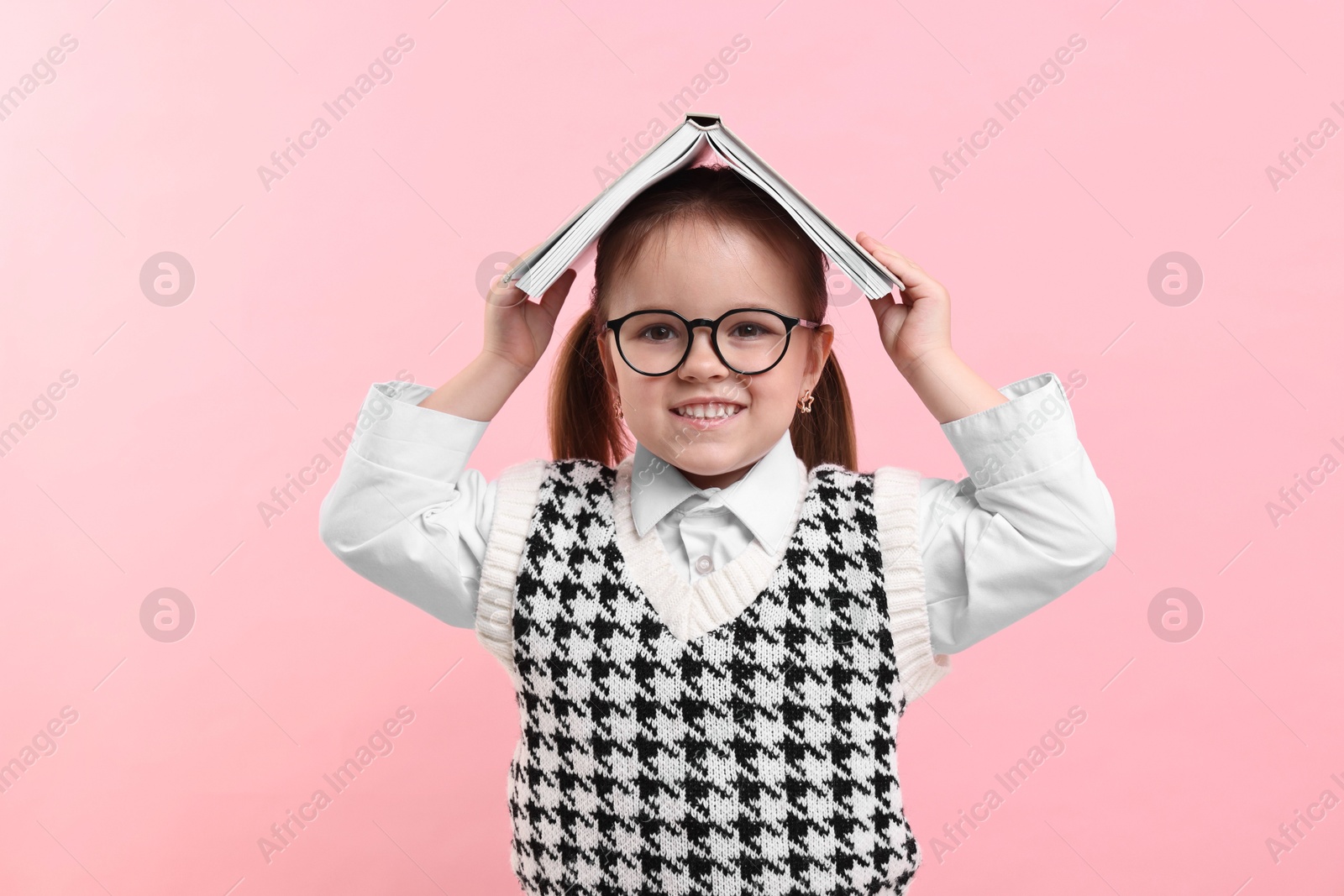 Photo of Cute little girl in glasses with open book on pink background