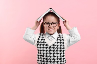 Cute little girl in glasses with open book on pink background