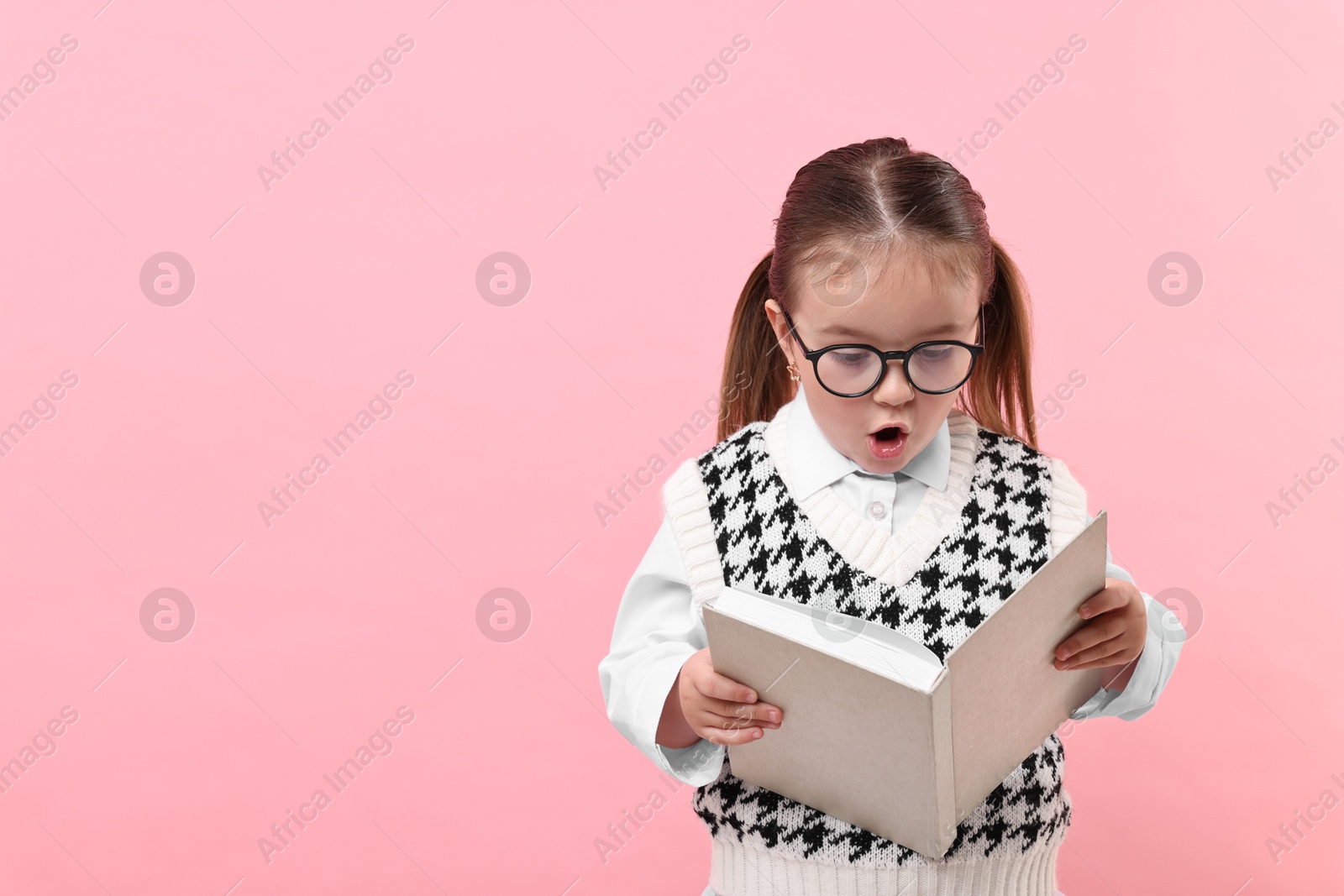 Photo of Emotional girl in glasses reading book on pink background. Space for text