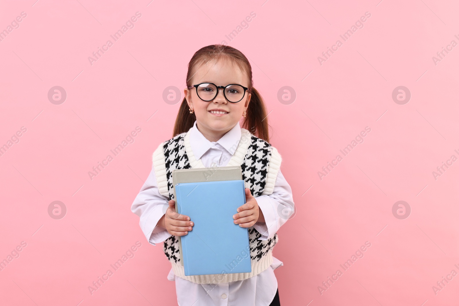 Photo of Cute little girl in glasses with books on pink background