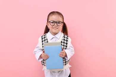 Cute little girl in glasses with books on pink background