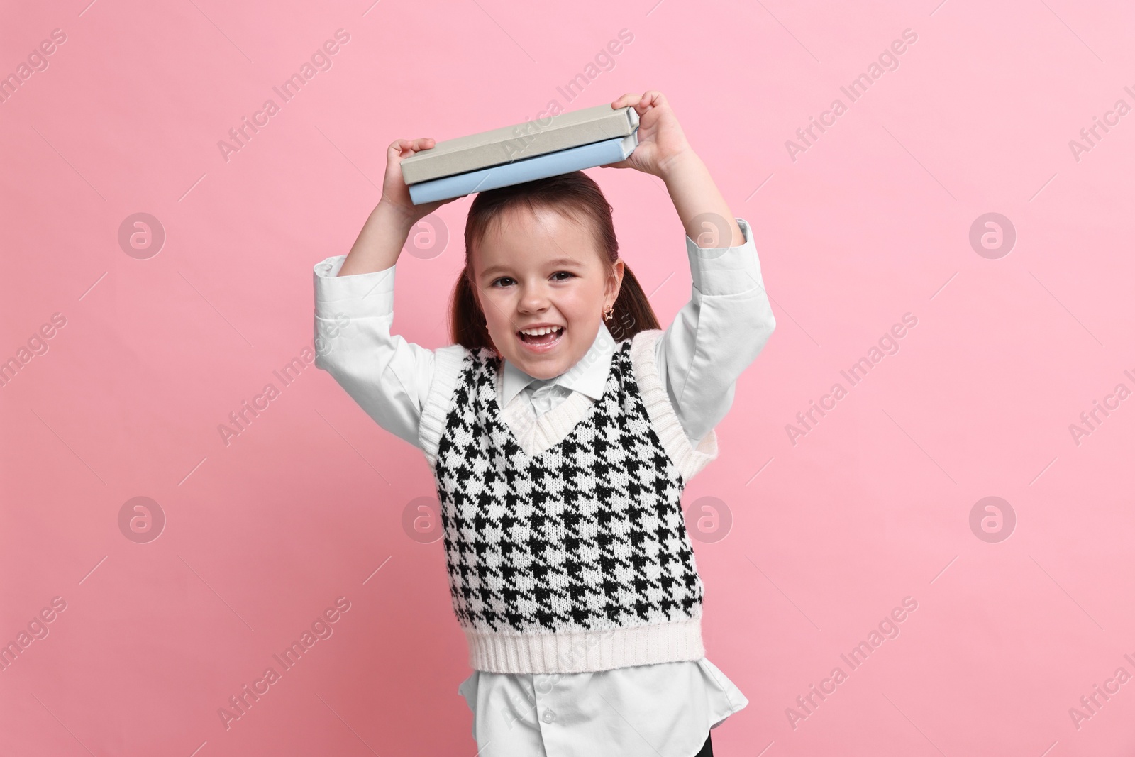 Photo of Cute little girl with books on pink background