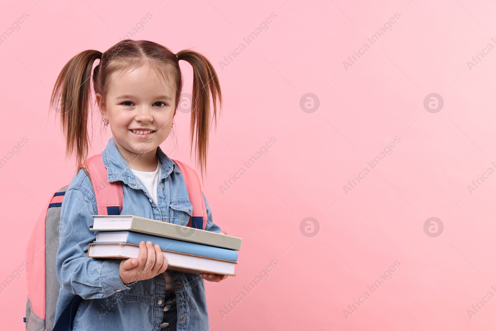 Photo of Cute little girl with books and backpack on pink background. Space for text