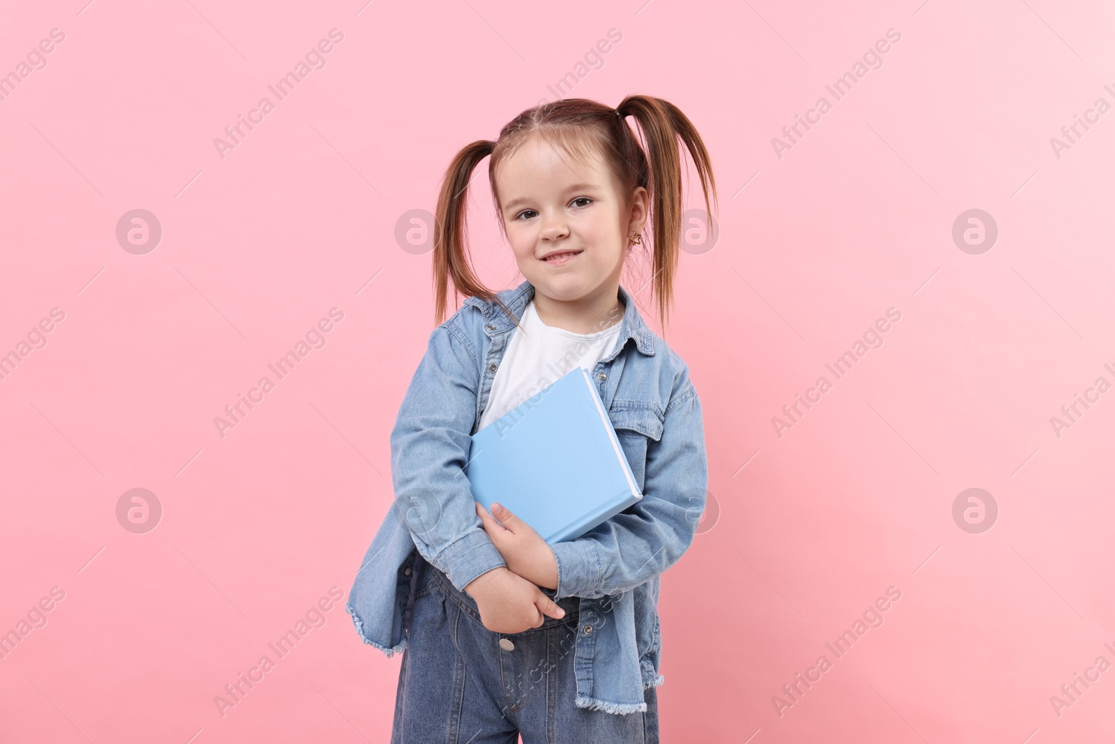 Photo of Cute little girl with book on pink background