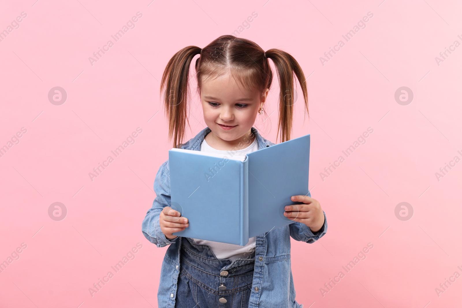 Photo of Cute little girl reading book on pink background