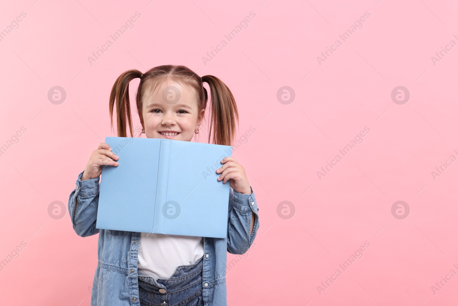 Photo of Cute little girl with book on pink background. Space for text