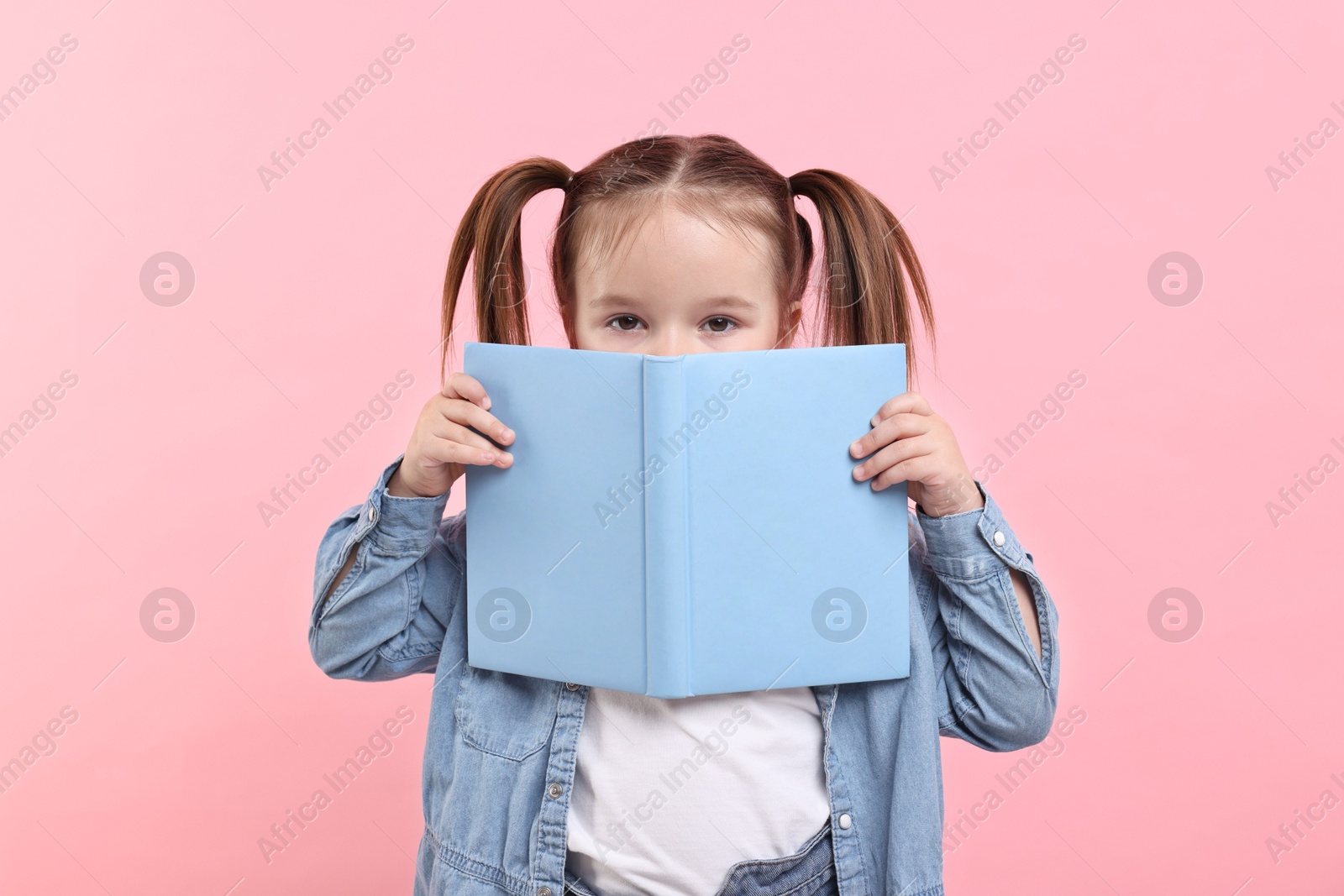 Photo of Cute little girl with open book on pink background