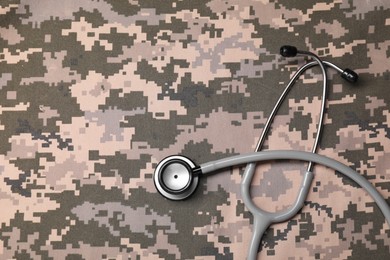 Stethoscope on camouflage fabric, top view. Space for text