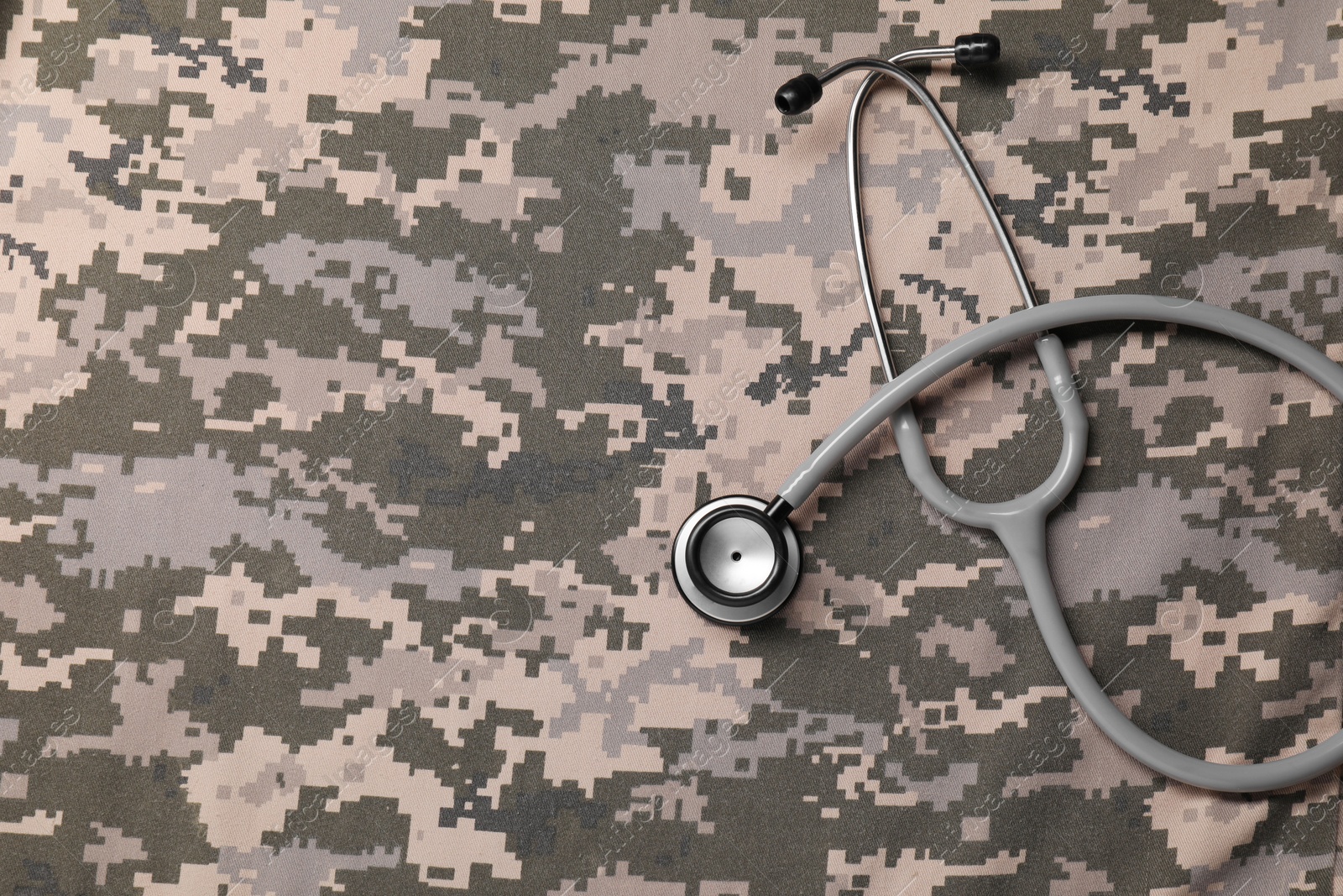 Photo of Stethoscope on camouflage fabric, top view. Space for text