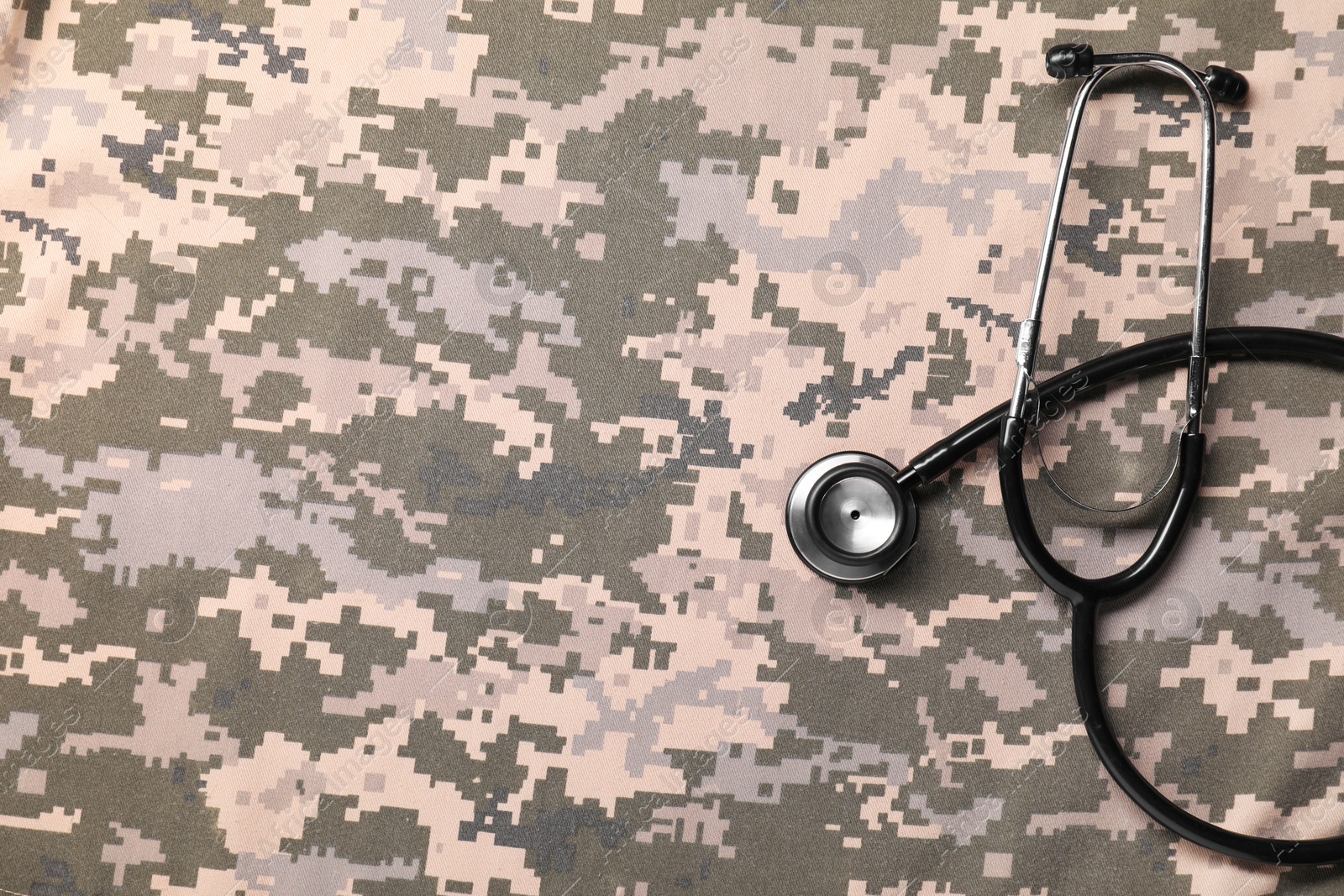 Photo of Stethoscope on camouflage fabric, top view. Space for text