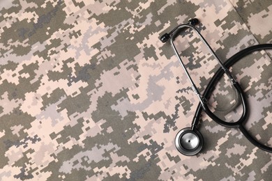 Photo of Stethoscope on camouflage fabric, top view. Space for text
