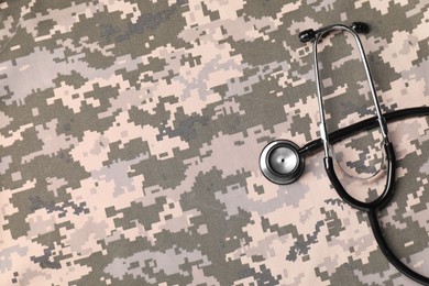 Stethoscope on camouflage fabric, top view. Space for text