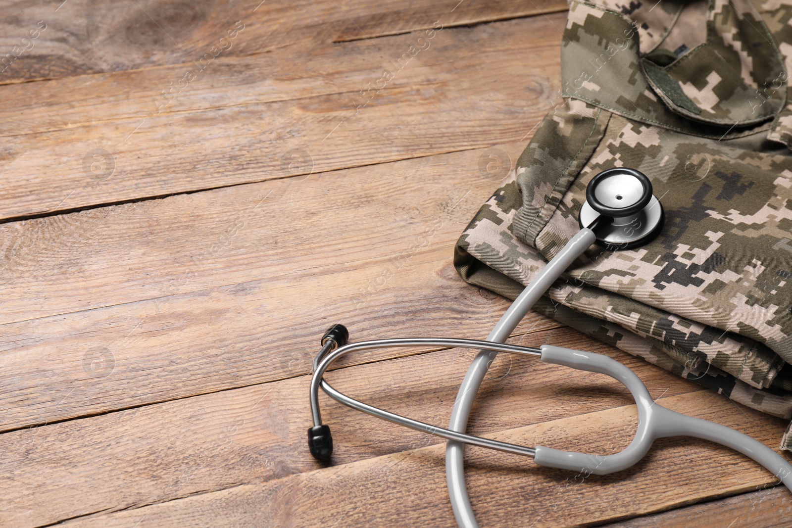 Photo of Stethoscope and military uniform on wooden table, space for text