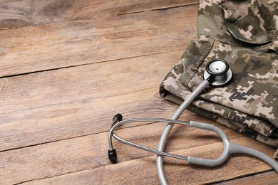 Stethoscope and military uniform on wooden table, space for text