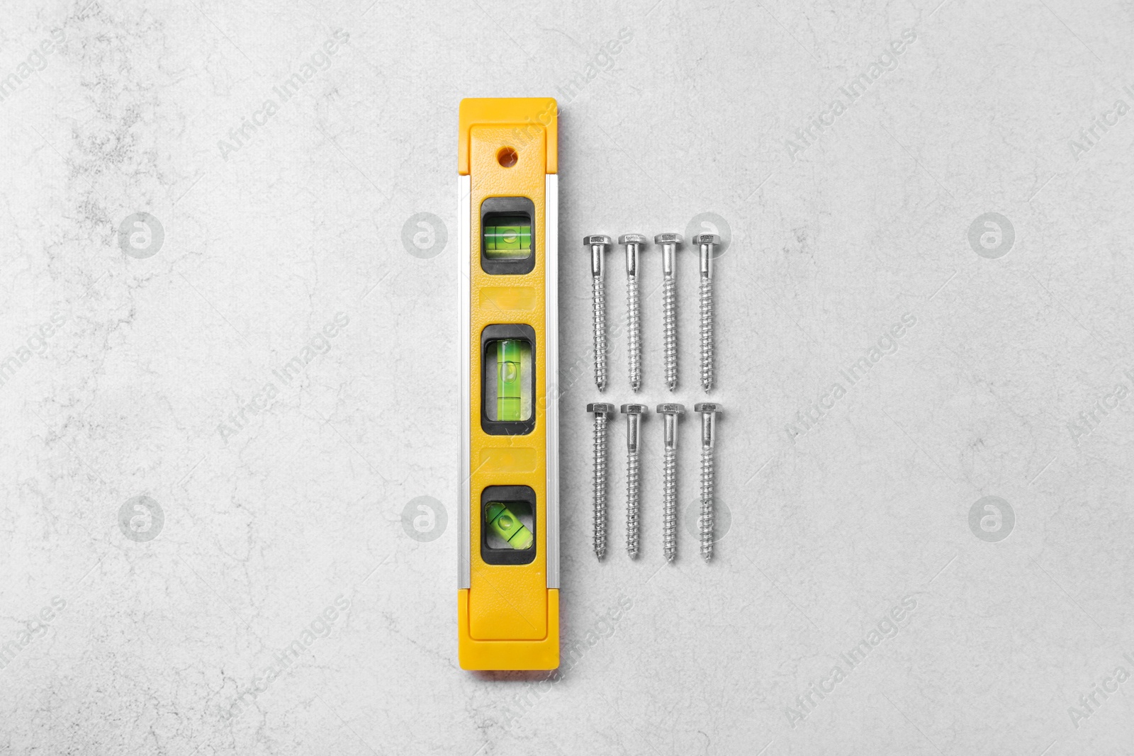 Photo of Yellow building level and screws on grey table, flat lay. Construction tool