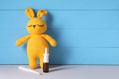 Photo of Toy bunny with nasal spray and thermometer on grey table near light blue wooden wall, space for text