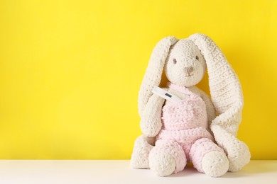 Photo of Toy bunny with thermometer on color background, space for text