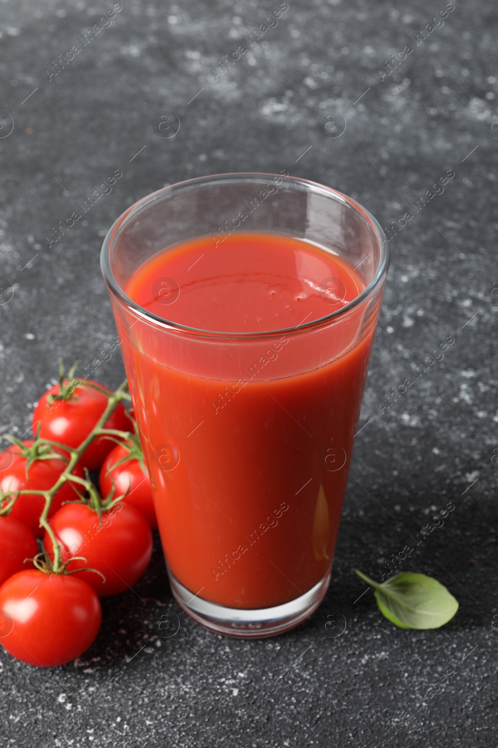 Photo of Tasty tomato juice in glass, basil and fresh vegetables on grey table