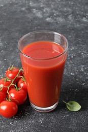 Photo of Tasty tomato juice in glass, basil and fresh vegetables on grey table