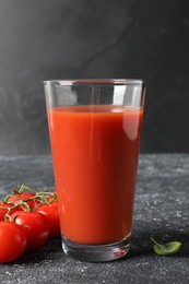 Photo of Tasty tomato juice in glass, basil and fresh vegetables on grey table