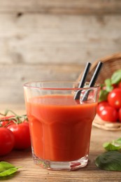 Photo of Tasty tomato juice in glass, basil leaves and fresh vegetables on wooden table