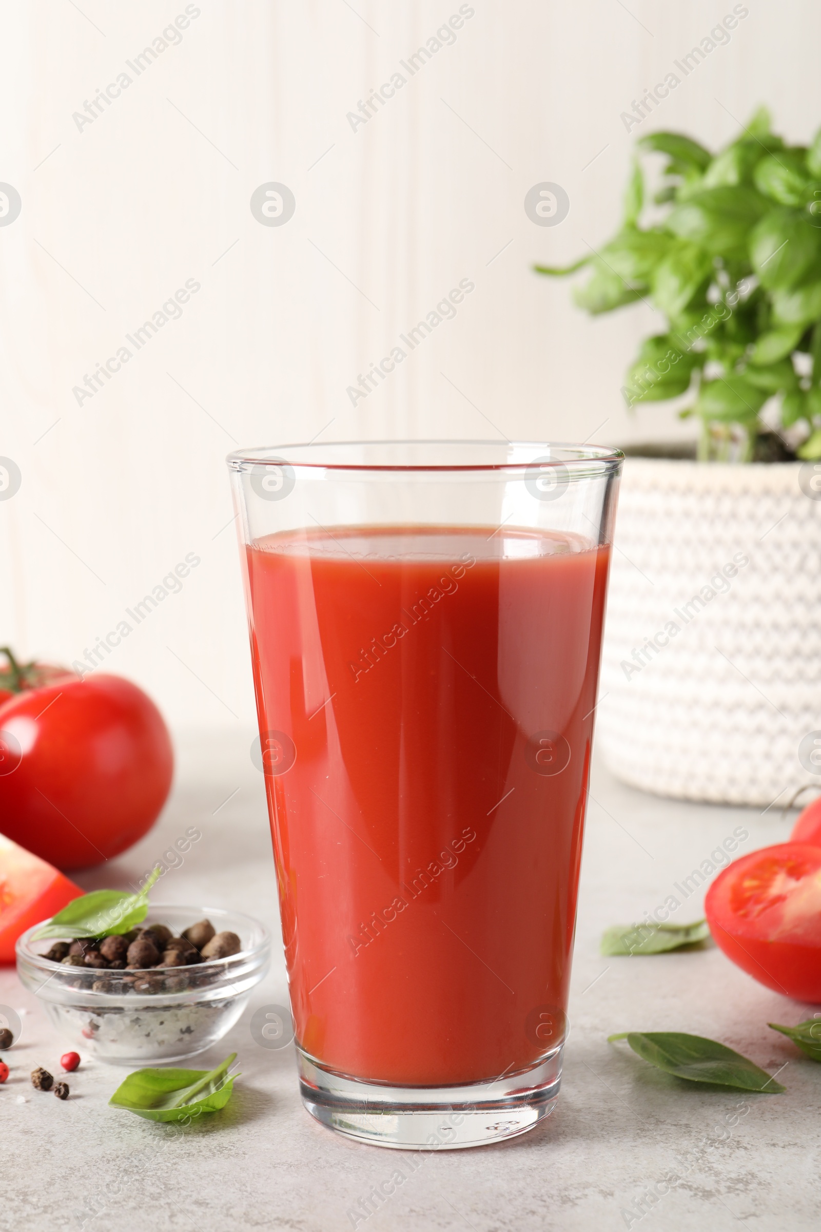 Photo of Tasty tomato juice in glass, basil leaves, peppercorns and fresh vegetables on light grey table