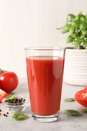 Tasty tomato juice in glass, basil leaves, peppercorns and fresh vegetables on light grey table