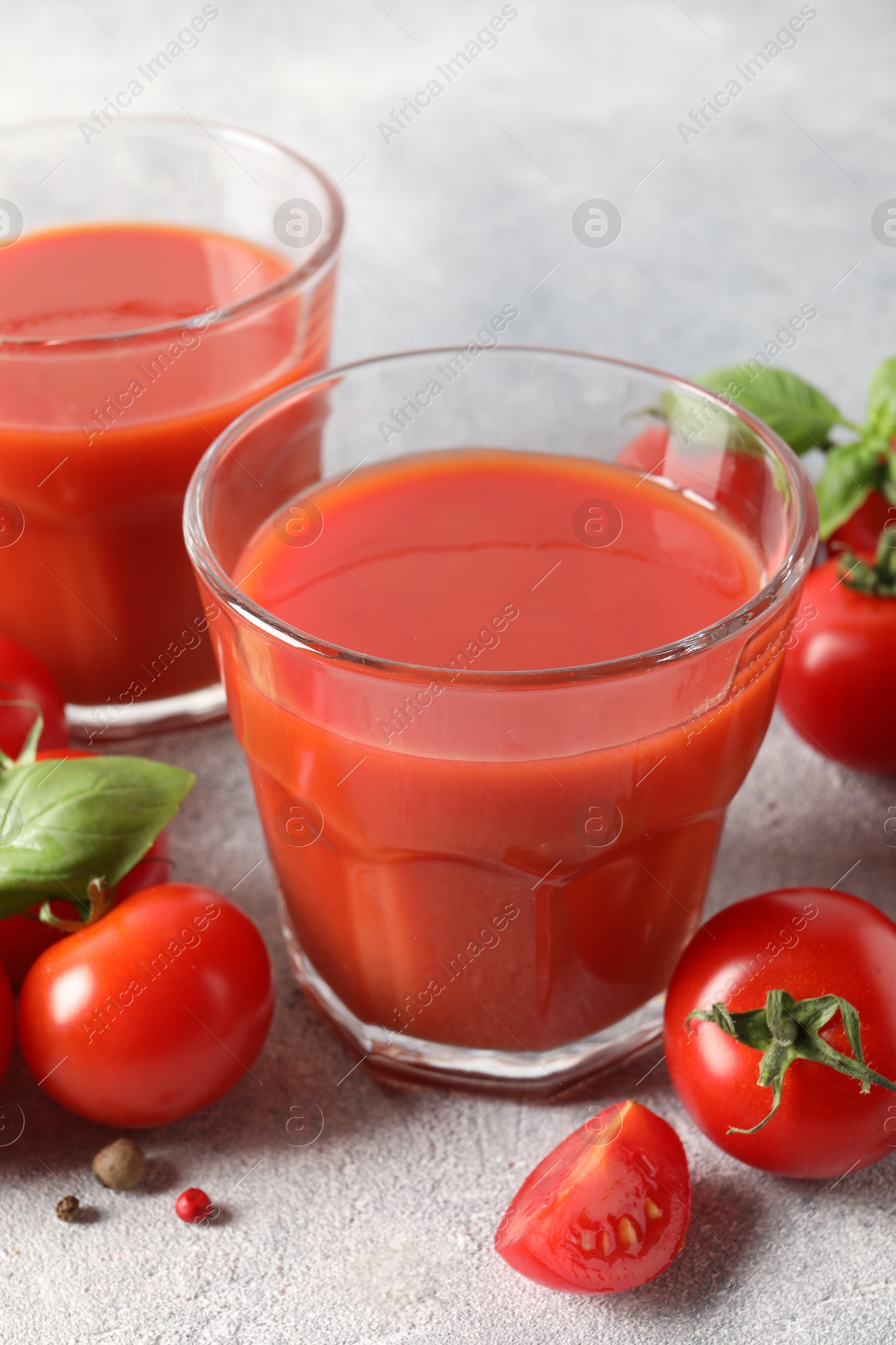 Photo of Tasty tomato juice in glasses, basil leaves, fresh vegetables and peppercorns on light grey table