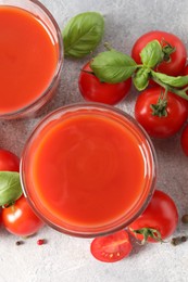 Photo of Tasty tomato juice in glasses, basil leaves, fresh vegetables and peppercorns on light grey table, flat lay