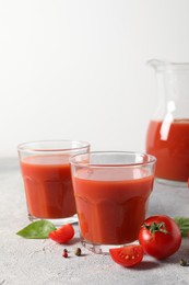 Photo of Tasty tomato juice in glasses, basil, peppercorns and fresh vegetables on light grey table