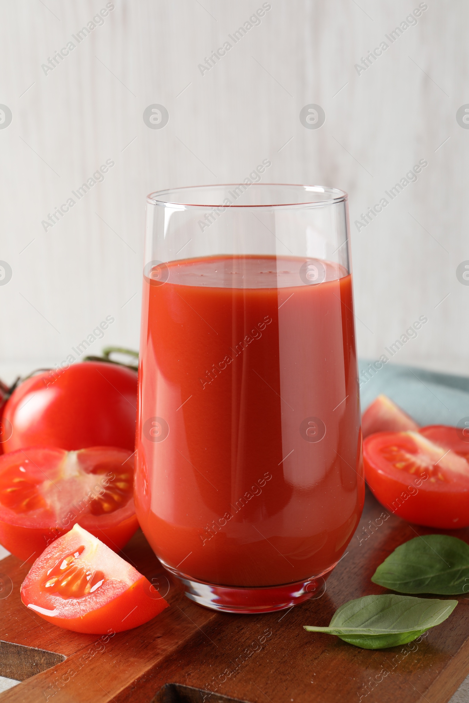 Photo of Tasty tomato juice in glass, basil leaves and fresh vegetables on table