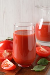 Photo of Tasty tomato juice in glass, basil leaves and fresh vegetables on table